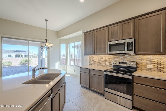 kitchen with backsplash, sink, light stone countertops, appliances with stainless steel finishes, and a notable chandelier