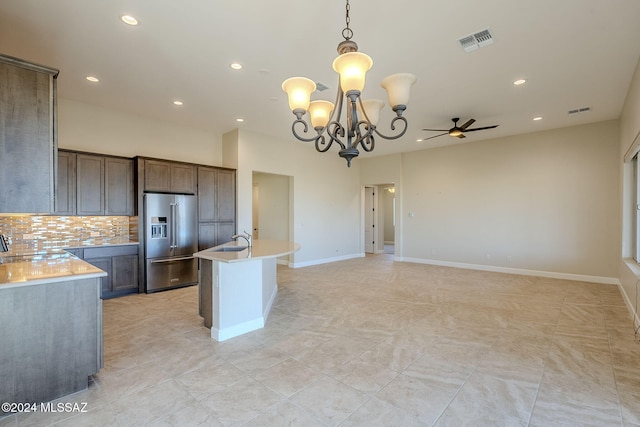 kitchen with decorative backsplash, high end fridge, ceiling fan with notable chandelier, a center island with sink, and hanging light fixtures