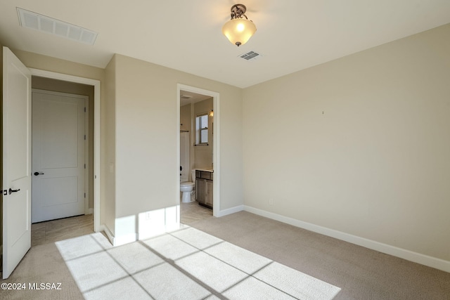 unfurnished bedroom featuring light carpet and ensuite bath