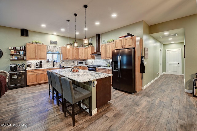 kitchen featuring pendant lighting, beverage cooler, a center island, black appliances, and wall chimney range hood