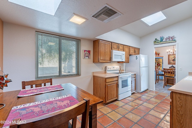 kitchen featuring lofted ceiling with skylight, a chandelier, white appliances, light tile patterned floors, and a textured ceiling