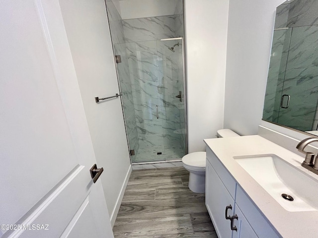bathroom with baseboards, toilet, vanity, wood finished floors, and a marble finish shower