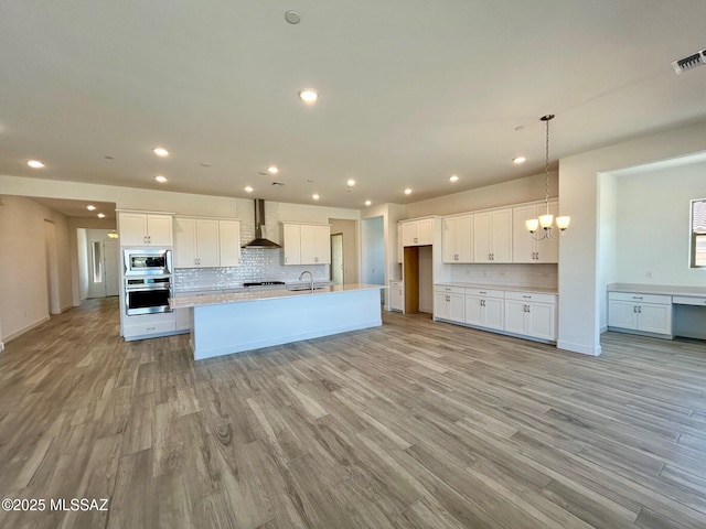 kitchen featuring white cabinetry, light wood-style floors, wall chimney exhaust hood, appliances with stainless steel finishes, and a sink