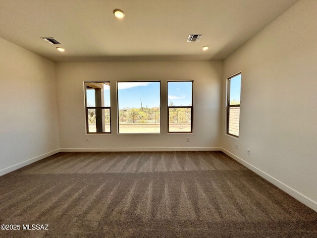empty room featuring visible vents, baseboards, and dark colored carpet