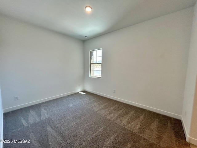 spare room featuring baseboards and dark colored carpet
