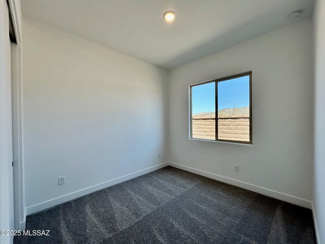 empty room with dark carpet and baseboards