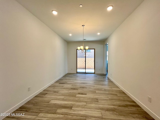 unfurnished dining area with light wood finished floors, a notable chandelier, and baseboards