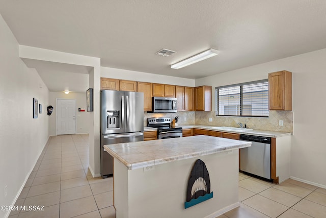 kitchen with a center island, backsplash, sink, light tile patterned floors, and appliances with stainless steel finishes