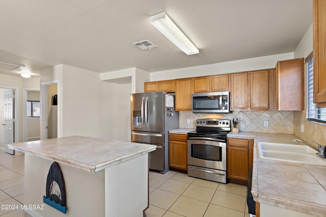 kitchen featuring backsplash, stainless steel appliances, sink, light tile patterned floors, and a center island