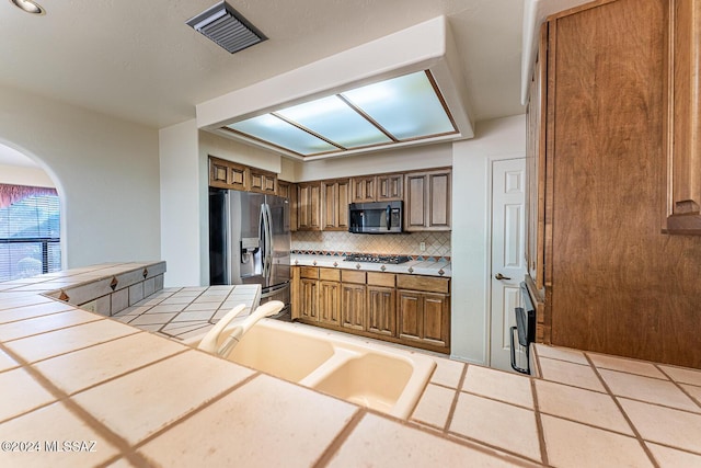 kitchen featuring tile counters, sink, decorative backsplash, light tile patterned floors, and appliances with stainless steel finishes