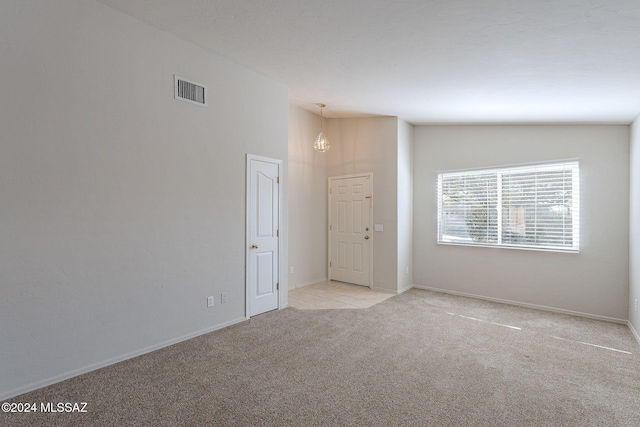 spare room featuring light carpet, an inviting chandelier, and lofted ceiling