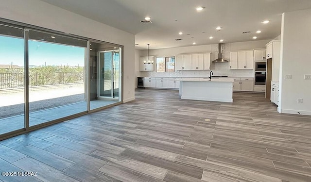 kitchen featuring light wood-type flooring, wall chimney exhaust hood, white cabinets, tasteful backsplash, and appliances with stainless steel finishes