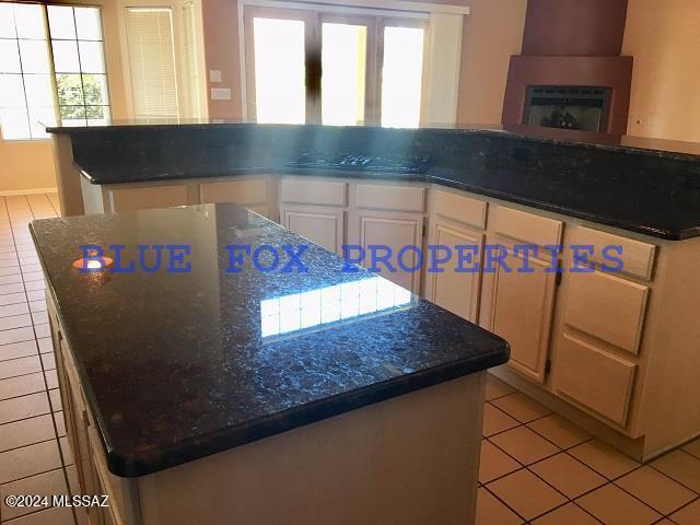 kitchen with white cabinetry, a center island, sink, dark stone counters, and light tile patterned flooring