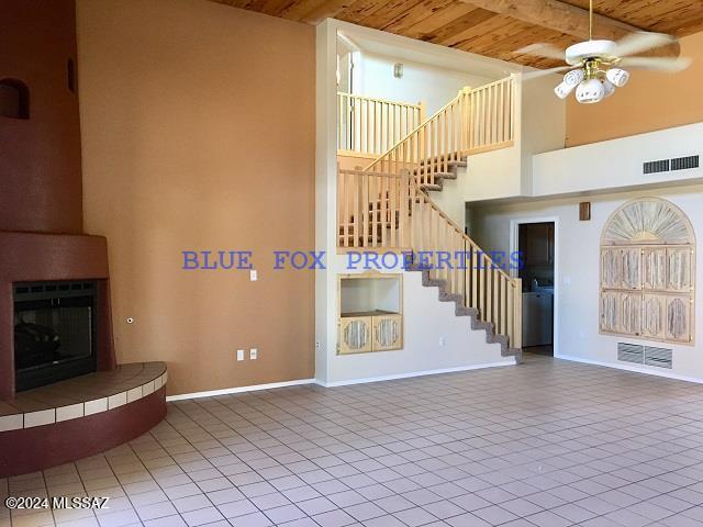 unfurnished living room featuring beam ceiling, ceiling fan, wooden ceiling, and a high ceiling