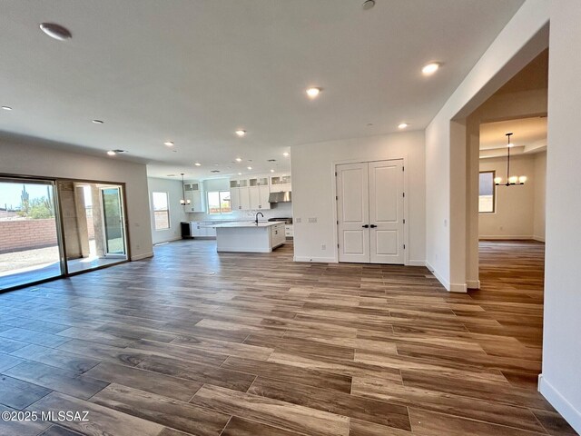 unfurnished living room with a chandelier, dark wood-style flooring, baseboards, and recessed lighting
