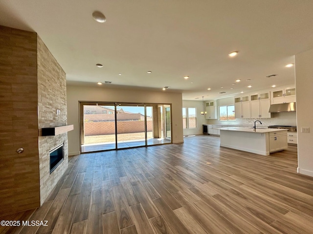 unfurnished living room featuring recessed lighting, a stone fireplace, a sink, and wood finished floors