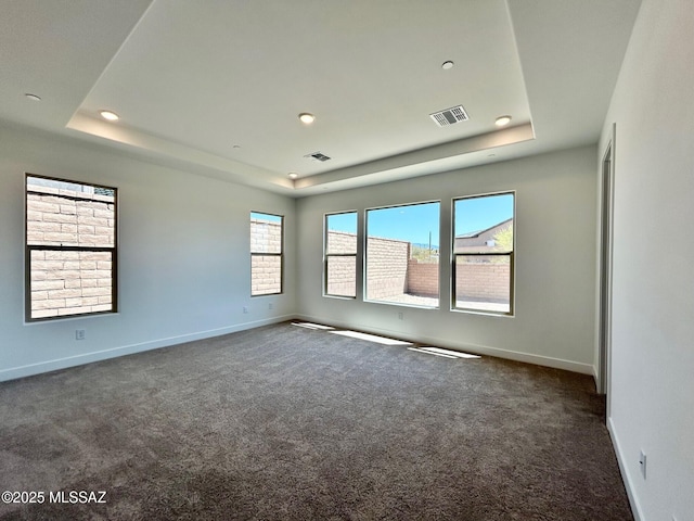spare room with visible vents, baseboards, a raised ceiling, and dark colored carpet