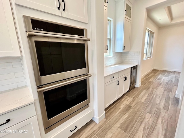 kitchen featuring double oven, light wood-type flooring, white cabinetry, wine cooler, and decorative backsplash