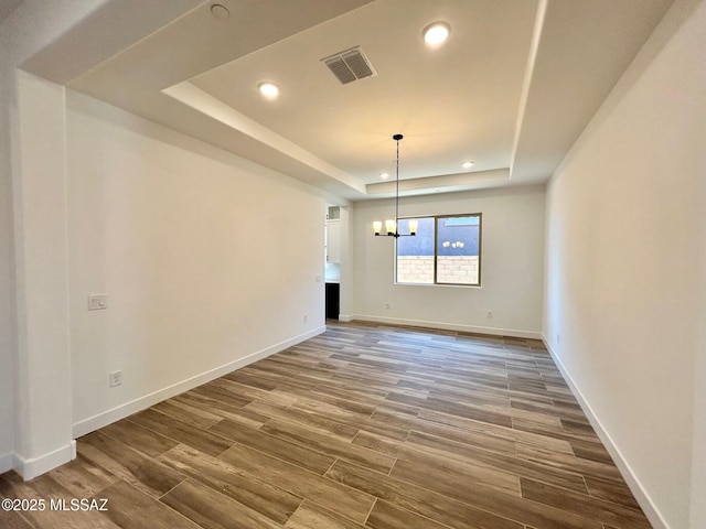 unfurnished dining area featuring visible vents, baseboards, wood finished floors, and a raised ceiling