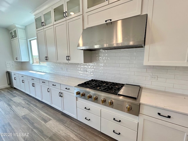 kitchen with light wood-type flooring, white cabinetry, under cabinet range hood, stainless steel gas cooktop, and decorative backsplash