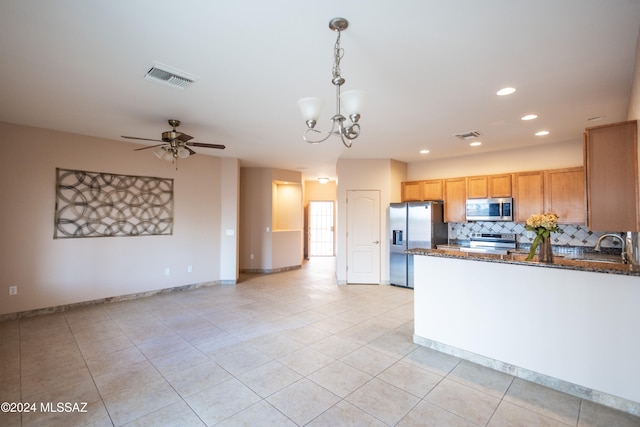 kitchen featuring pendant lighting, dark stone counters, ceiling fan with notable chandelier, decorative backsplash, and appliances with stainless steel finishes