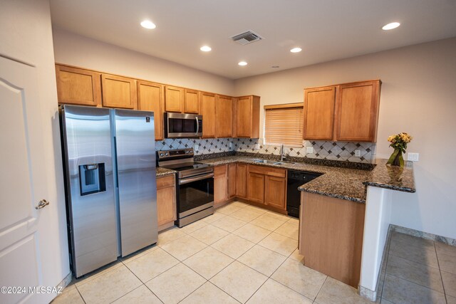 kitchen featuring decorative backsplash, appliances with stainless steel finishes, kitchen peninsula, dark stone counters, and sink