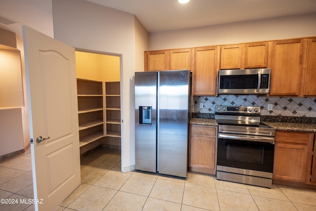 kitchen featuring decorative backsplash, light tile patterned floors, stainless steel appliances, and dark stone countertops