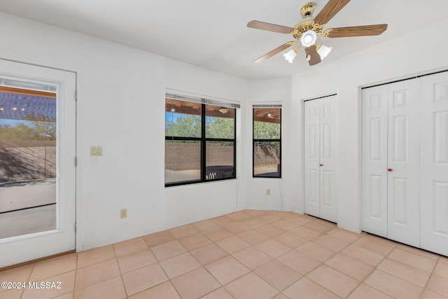 unfurnished bedroom with ceiling fan, light tile patterned floors, and multiple closets