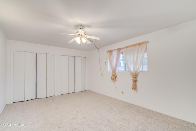 unfurnished bedroom with multiple closets, light colored carpet, and ceiling fan