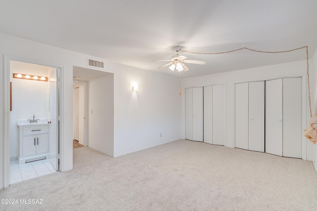 unfurnished bedroom with sink, ensuite bath, light carpet, two closets, and ceiling fan