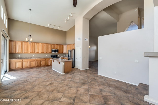 kitchen featuring stainless steel appliances, a towering ceiling, pendant lighting, a breakfast bar area, and a center island with sink