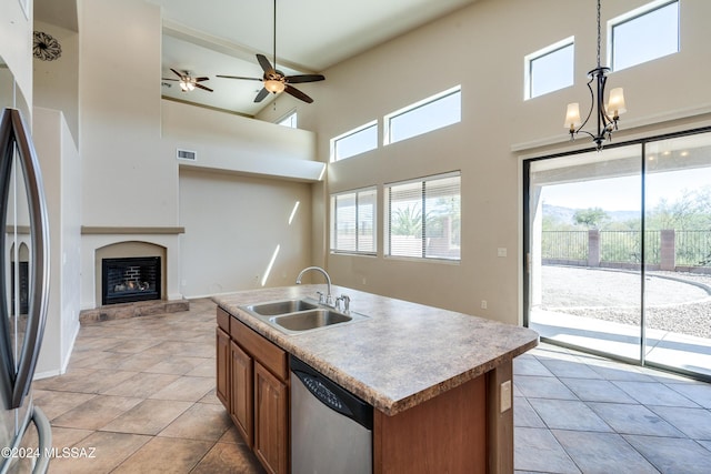 kitchen with appliances with stainless steel finishes, a towering ceiling, sink, a center island with sink, and hanging light fixtures