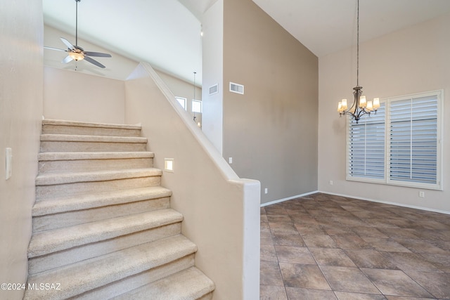 stairway with high vaulted ceiling and ceiling fan with notable chandelier