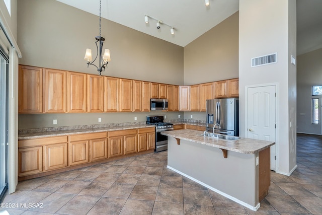 kitchen with a towering ceiling, stainless steel appliances, a kitchen island with sink, a chandelier, and hanging light fixtures