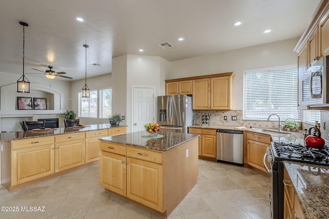 kitchen with appliances with stainless steel finishes, decorative light fixtures, sink, dark stone countertops, and a center island