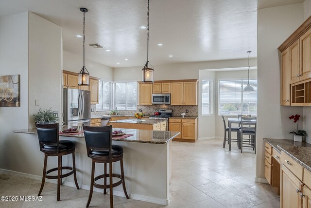 kitchen with appliances with stainless steel finishes, decorative backsplash, a kitchen bar, decorative light fixtures, and dark stone counters