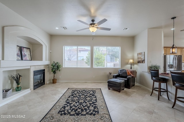 sitting room featuring built in shelves, a tile fireplace, and ceiling fan