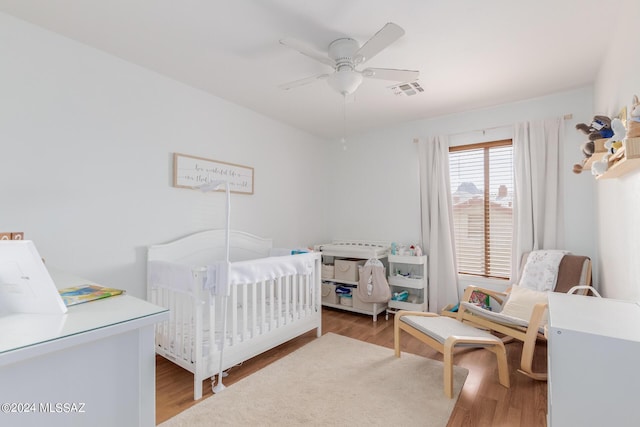 bedroom with ceiling fan, a crib, and hardwood / wood-style floors