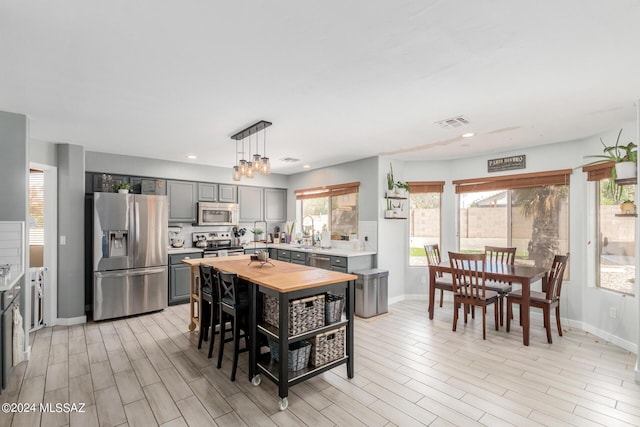 kitchen with decorative light fixtures, appliances with stainless steel finishes, a wealth of natural light, and gray cabinets