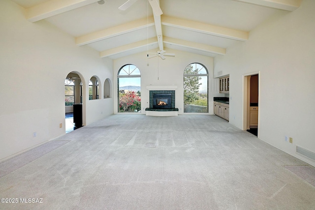 unfurnished living room with light carpet, beamed ceiling, ceiling fan, and high vaulted ceiling