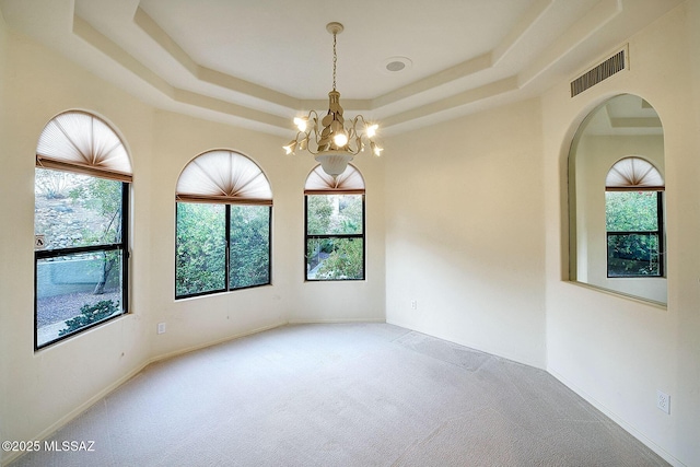 empty room with a tray ceiling, carpet floors, and a chandelier