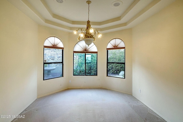 carpeted spare room with a tray ceiling and an inviting chandelier