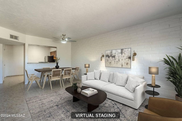 living room with a textured ceiling, ceiling fan, and brick wall