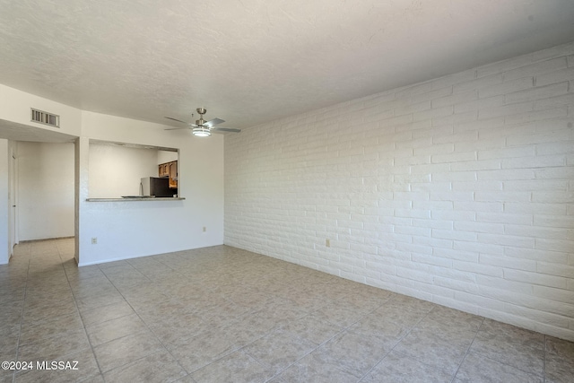 unfurnished living room featuring ceiling fan, brick wall, and a textured ceiling