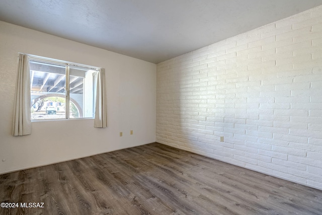 unfurnished room with hardwood / wood-style flooring and brick wall