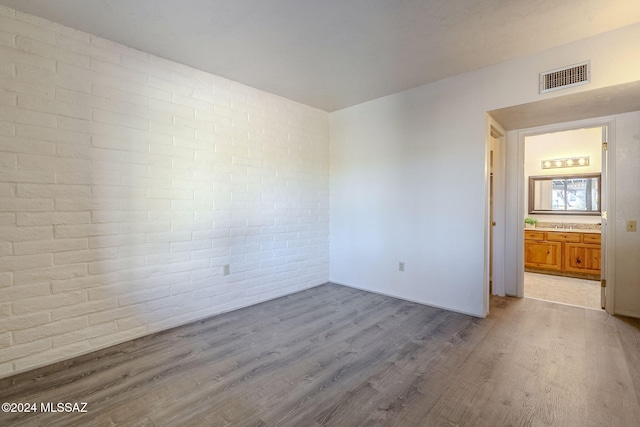 unfurnished room featuring brick wall and light wood-type flooring