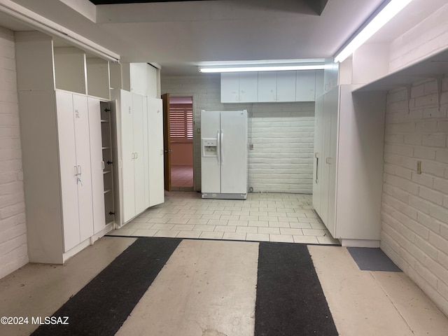 interior space with white cabinetry, light tile patterned floors, white refrigerator with ice dispenser, and brick wall