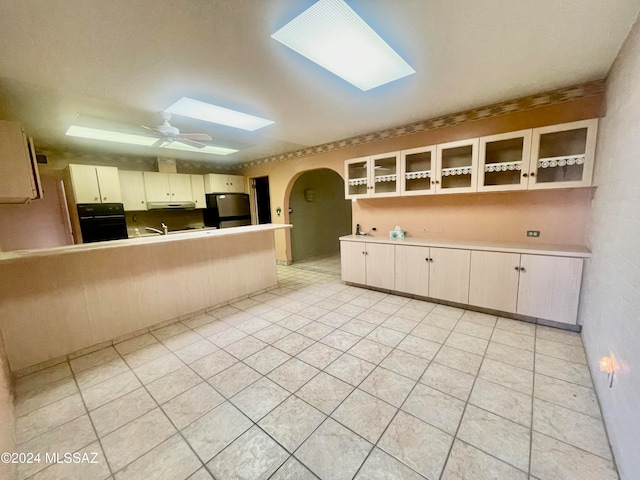 kitchen featuring a skylight, ceiling fan, black appliances, light tile patterned floors, and cream cabinets