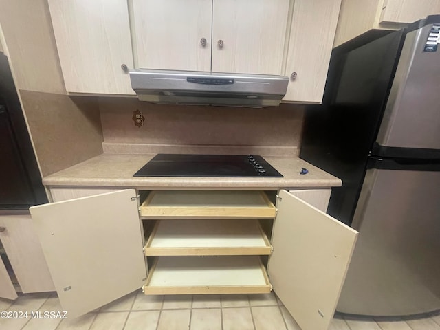 kitchen with light tile patterned floors, black electric cooktop, and stainless steel refrigerator