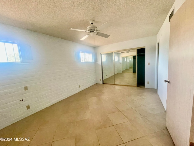 unfurnished bedroom with ceiling fan, a closet, brick wall, and multiple windows